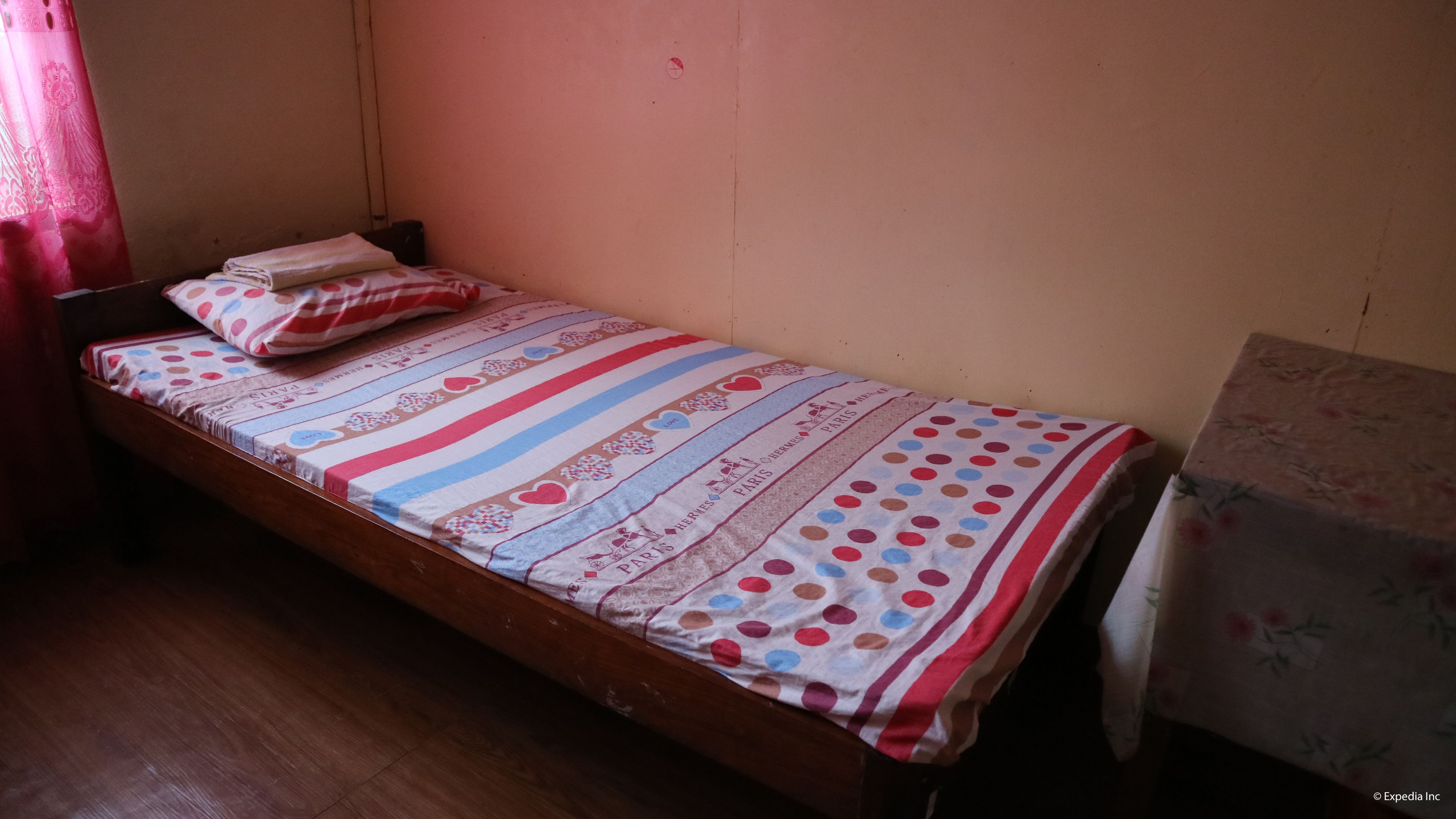 A single bed with a striped bedspread and pillows, a wooden headboard, and a plain wall.