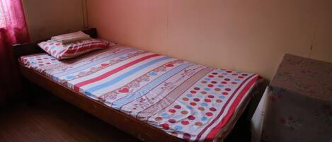 A single bed with a striped bedspread and pillows, a wooden headboard, and a plain wall.