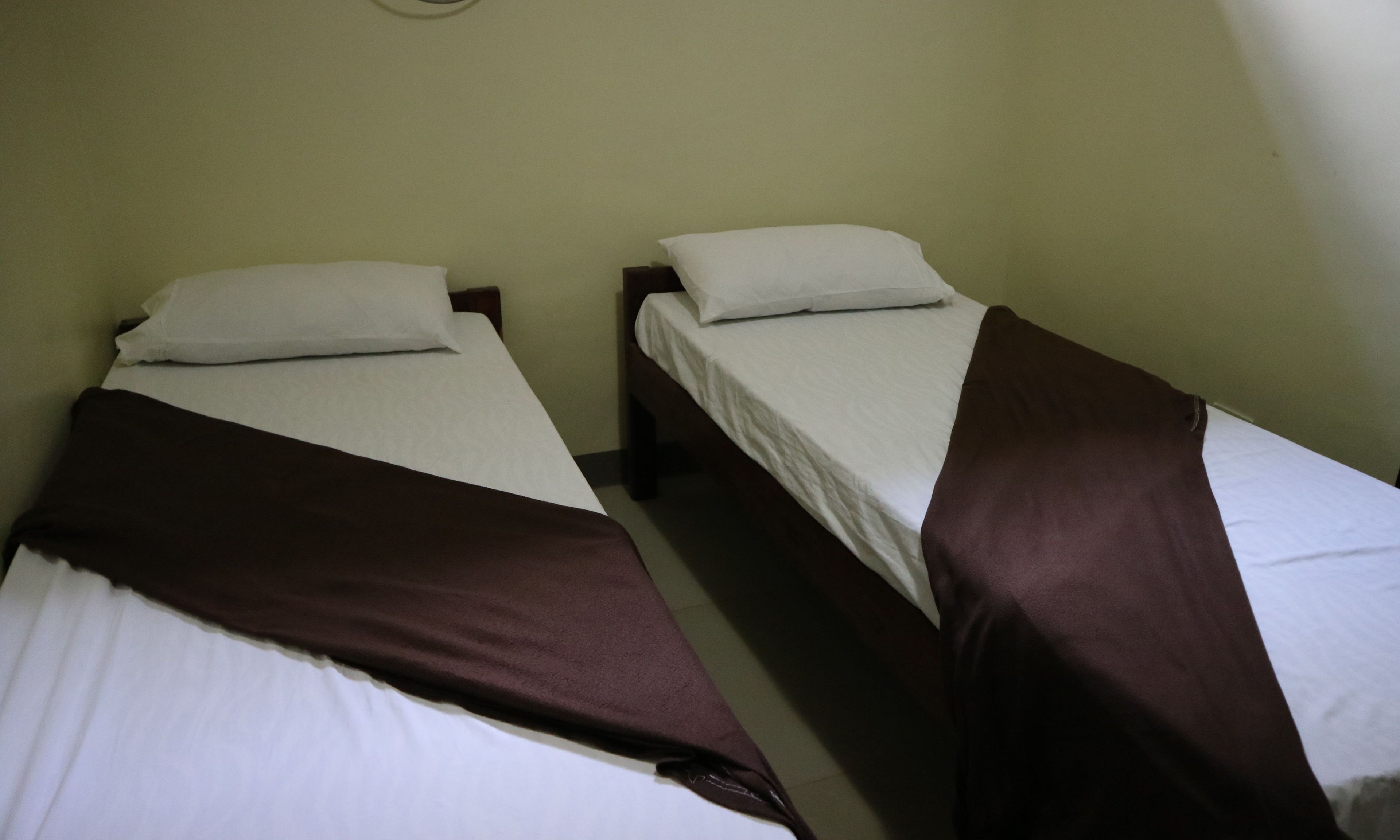 Two single beds with white linens and brown headboards in a room with plain walls.