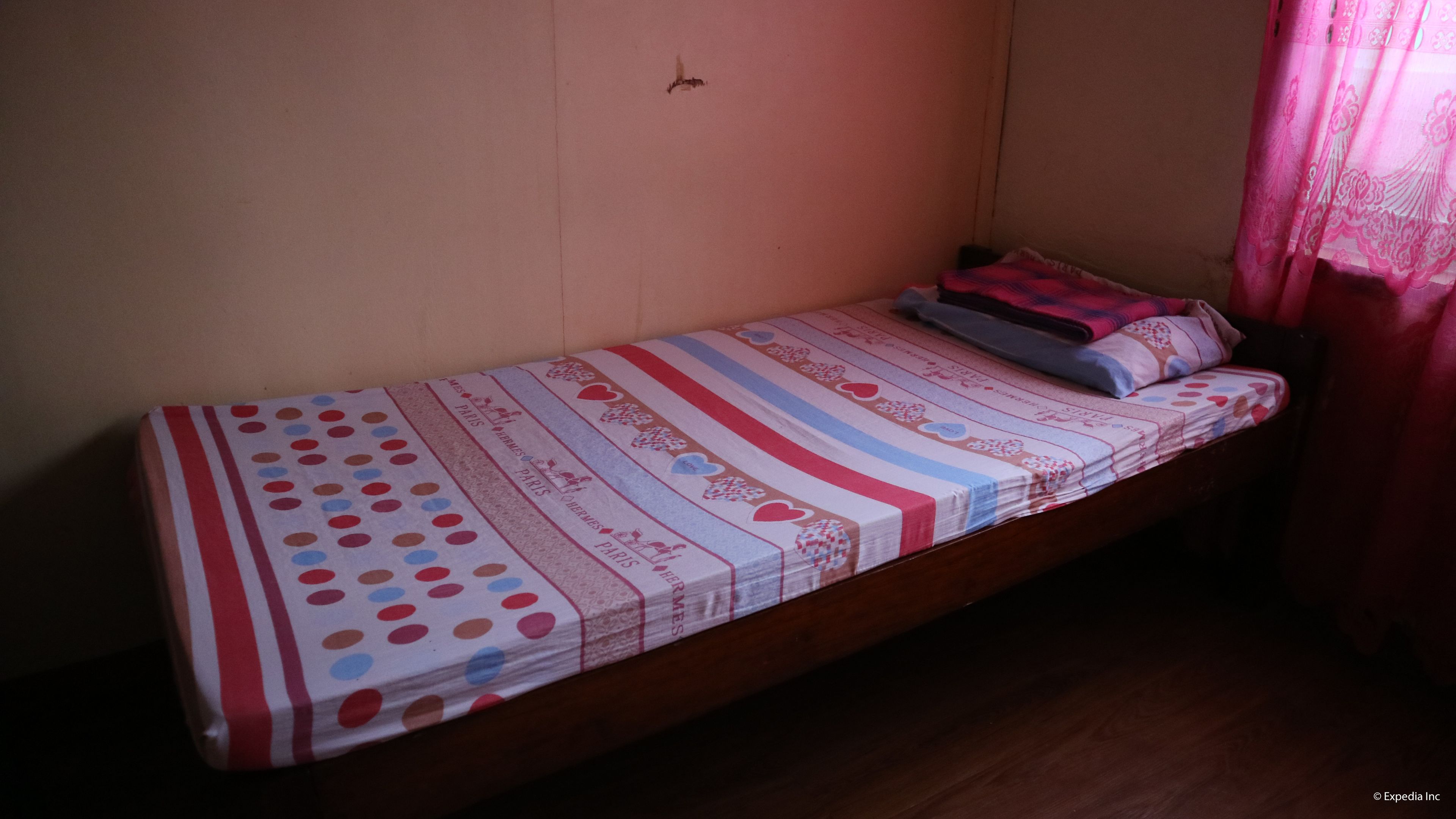 A single bed with a striped bedspread and pillows, a wooden headboard, and a small clock on the wall.