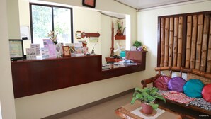 A reception area with a wooden desk, a computer, and a potted plant. - Mabini Pensione (Puerto Princesa)