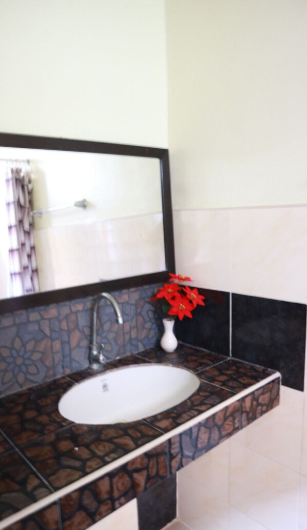 A bathroom with a stone-patterned sink, a mirror, and a vase with red flowers.
