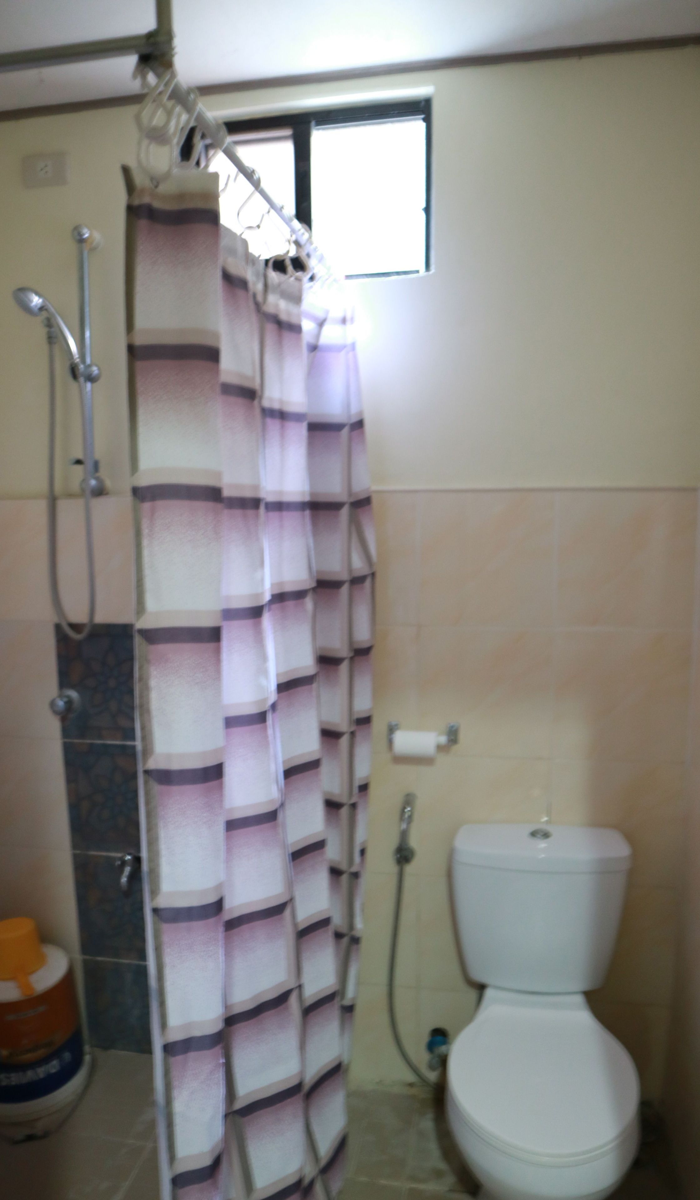 A bathroom with a shower curtain, a toilet, and a window.