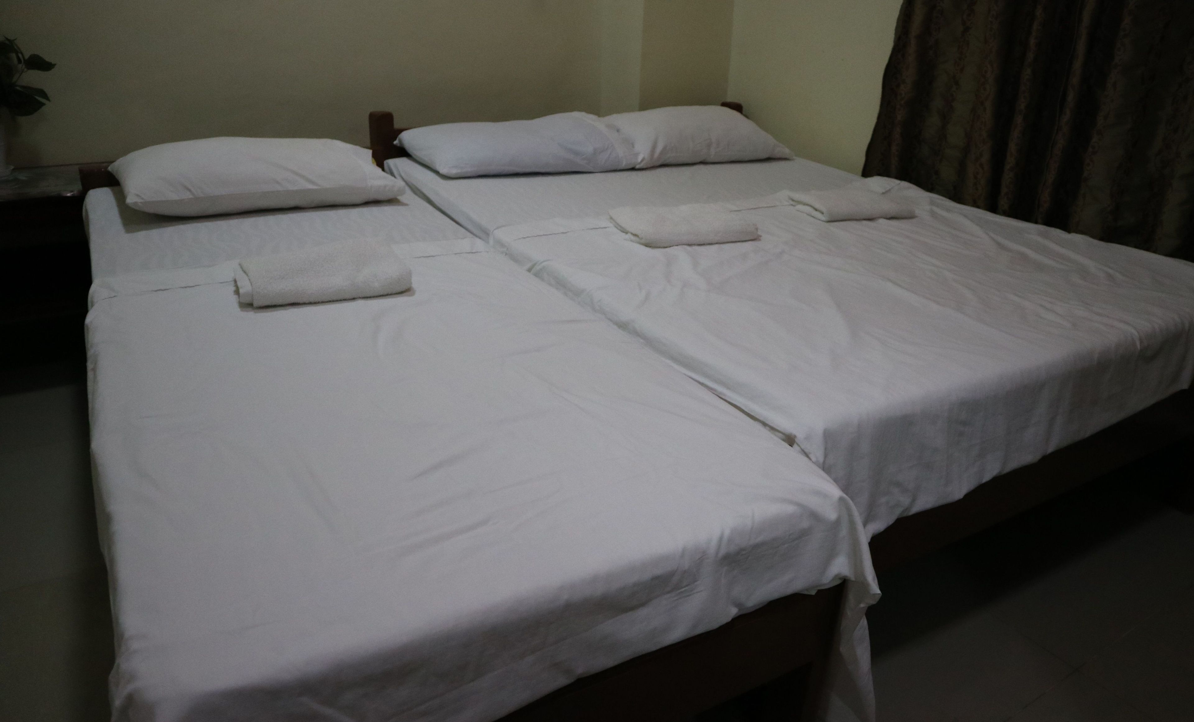 A hotel room with two single beds, each with white linens and pillows, and a wooden headboard.
