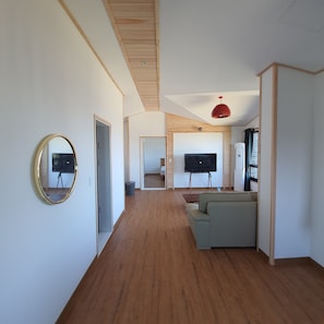 A spacious living area with a wooden floor, a grey sofa, a flat-screen TV, and a red pendant light. - On The Stone Pension (Seogwipo)