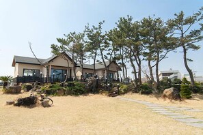 A modern house with a stone pathway leading to the entrance, surrounded by pine trees and landscaped garden. - On The Stone Pension (Seogwipo)
