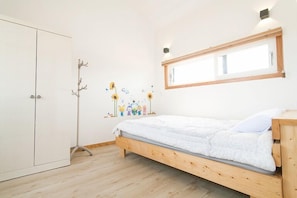 A bedroom with a wooden bed, a wardrobe, a coat rack, and a wall-mounted mirror.
