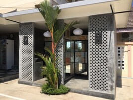 Entrada de un edificio moderno con una palmera, una máquina expendedora y un muro con diseño.