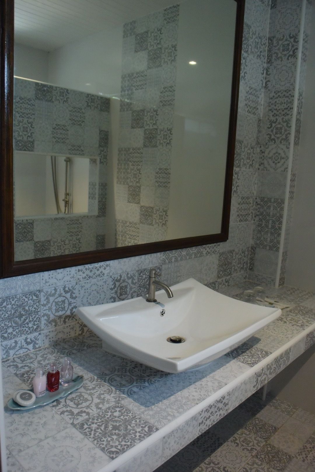 Un baño con un lavamanos blanco, un espejo y baldosas estampadas.