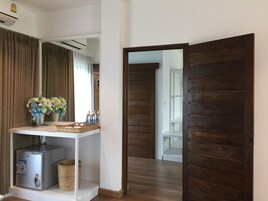 Habitación de hotel con una puerta de madera, una mesita consola blanca con espejo y un refrigerador pequeño.