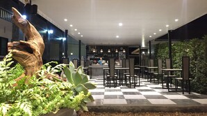 An indoor dining area with a checkered floor, potted plants, and a wooden sculpture. - Phetcharat Grand Hotel Maesot (Mae Sot)