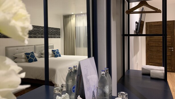 A hotel room with a bed, a wooden door, a hanging coat rack, and a table with bottles and glasses. - Phetcharat Grand Hotel Maesot (Mae Sot)