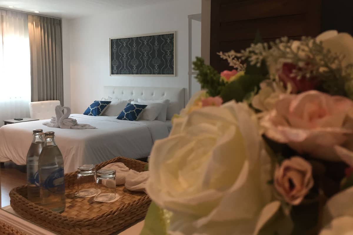 Une chambre d’hôtel comprenant un lit, une table de chevet avec une bouteille et des verres, un élément décoratif mural et un arrangement floral.