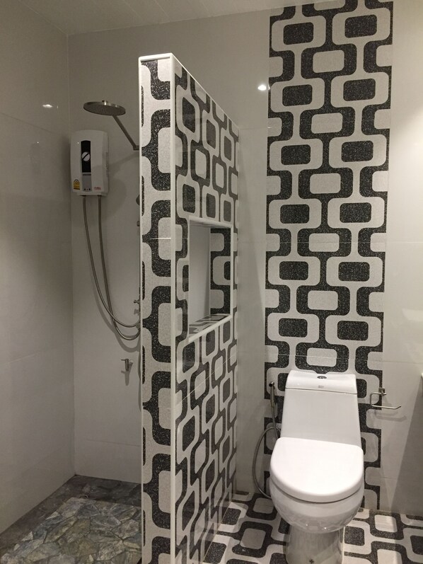 A bathroom with a patterned wall, a toilet, and a shower enclosure. - Phetcharat Grand Hotel Maesot (Mae Sot)