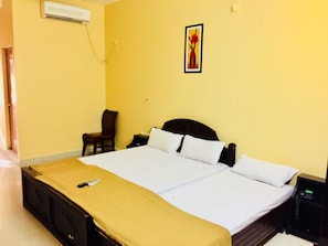 Un letto matrimoniale con copriletto beige, un comodino con lampada, una sedia e un condizionatore d'aria a muro.