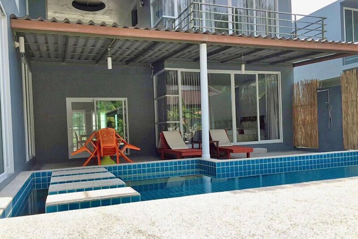 A modern pool area with a clear blue pool, a covered patio with lounge chairs, and a view of the surrounding landscape.