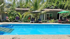 A swimming pool with lounge chairs and umbrellas, surrounded by palm trees and a building with a tiled roof. - Cousin Resort Koh Kho Khao Beach (Takua Pa)