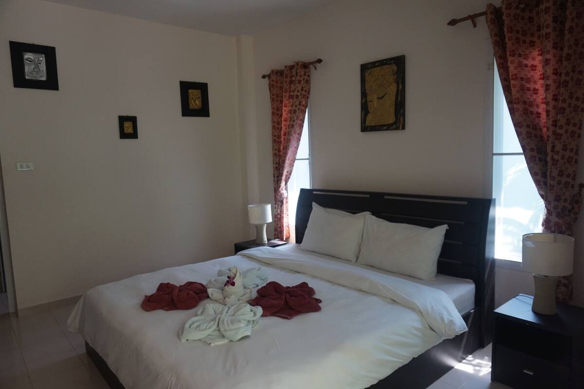 A hotel room with a bed, two bedside tables with lamps, a window with curtains, and wall art.