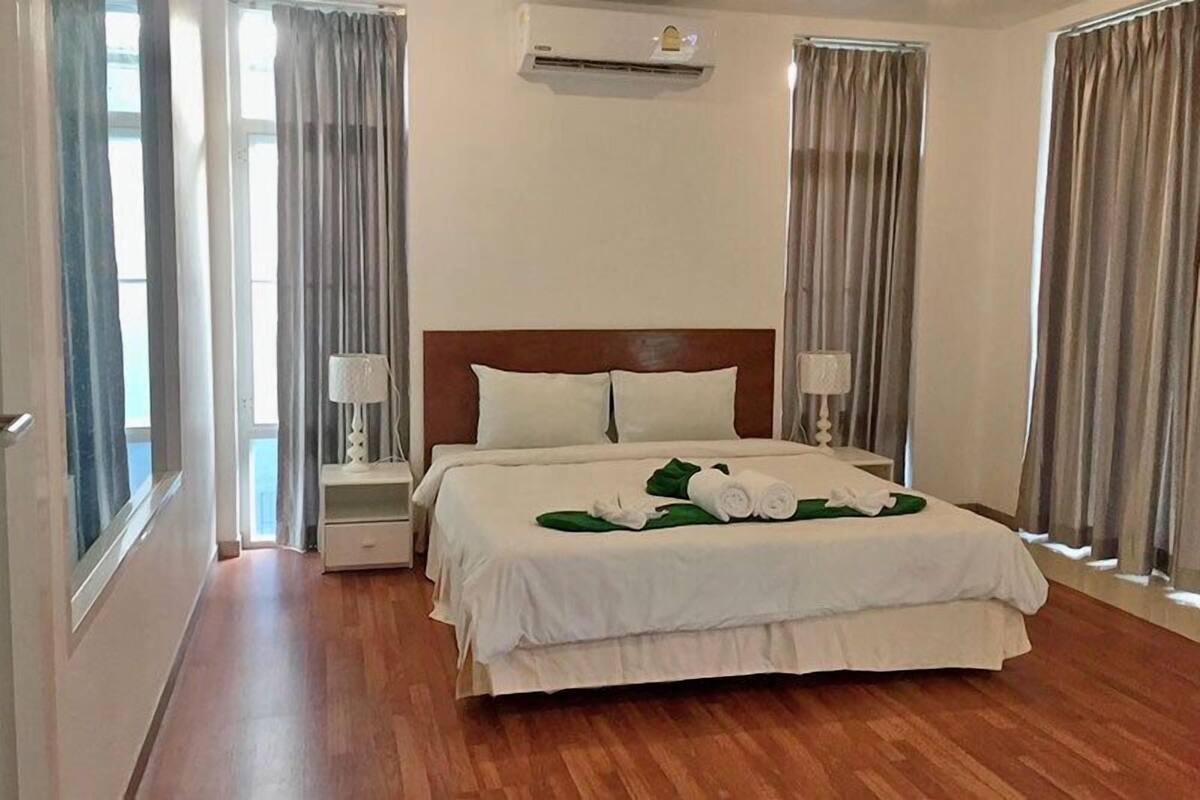 A hotel room with a wooden floor, a bed with white bedding, two bedside lamps, and a window with curtains.