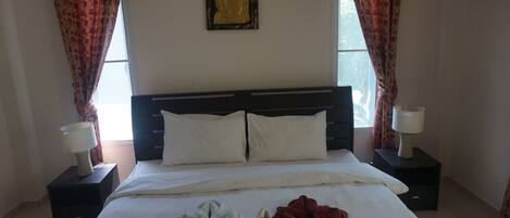Una habitación de hotel con una cama, dos mesitas de noche con lámparas, una estatua de Buda en la pared y cortinas.