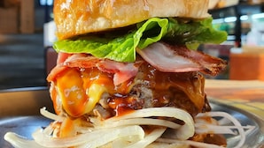 Una hamburguesa con lechuga, tocino y queso fundido en un pan, acompañada de aros de cebolla.