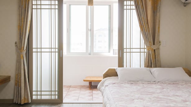 Un dormitorio con cama, una ventana con cortinas, un banco de madera y un equipo de aire acondicionado.