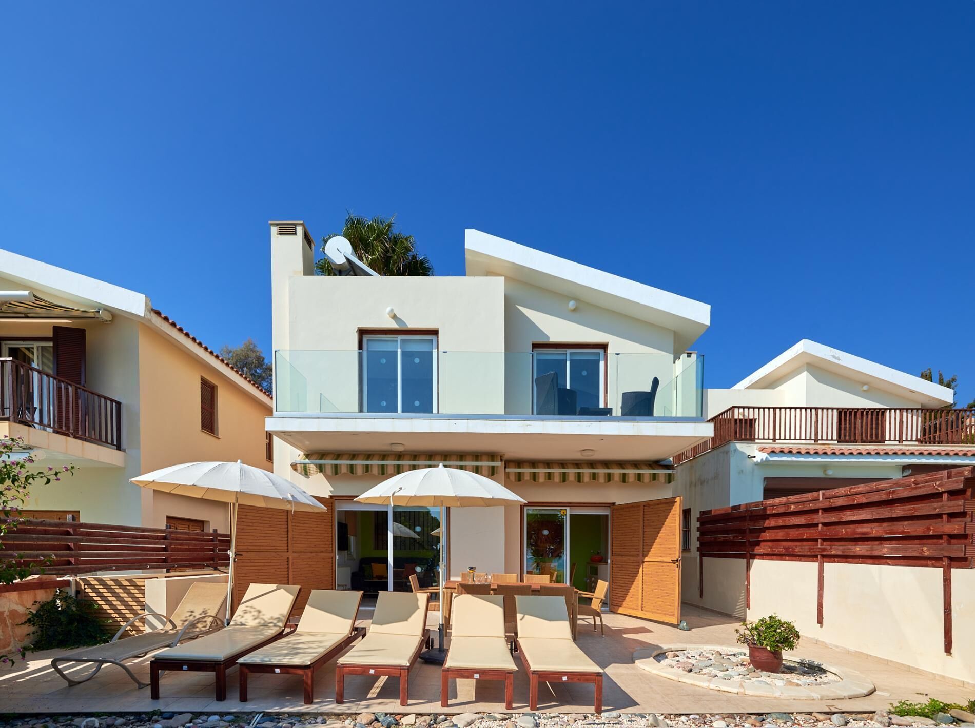 A modern two-story house with a balcony, outdoor seating area, and a pool.