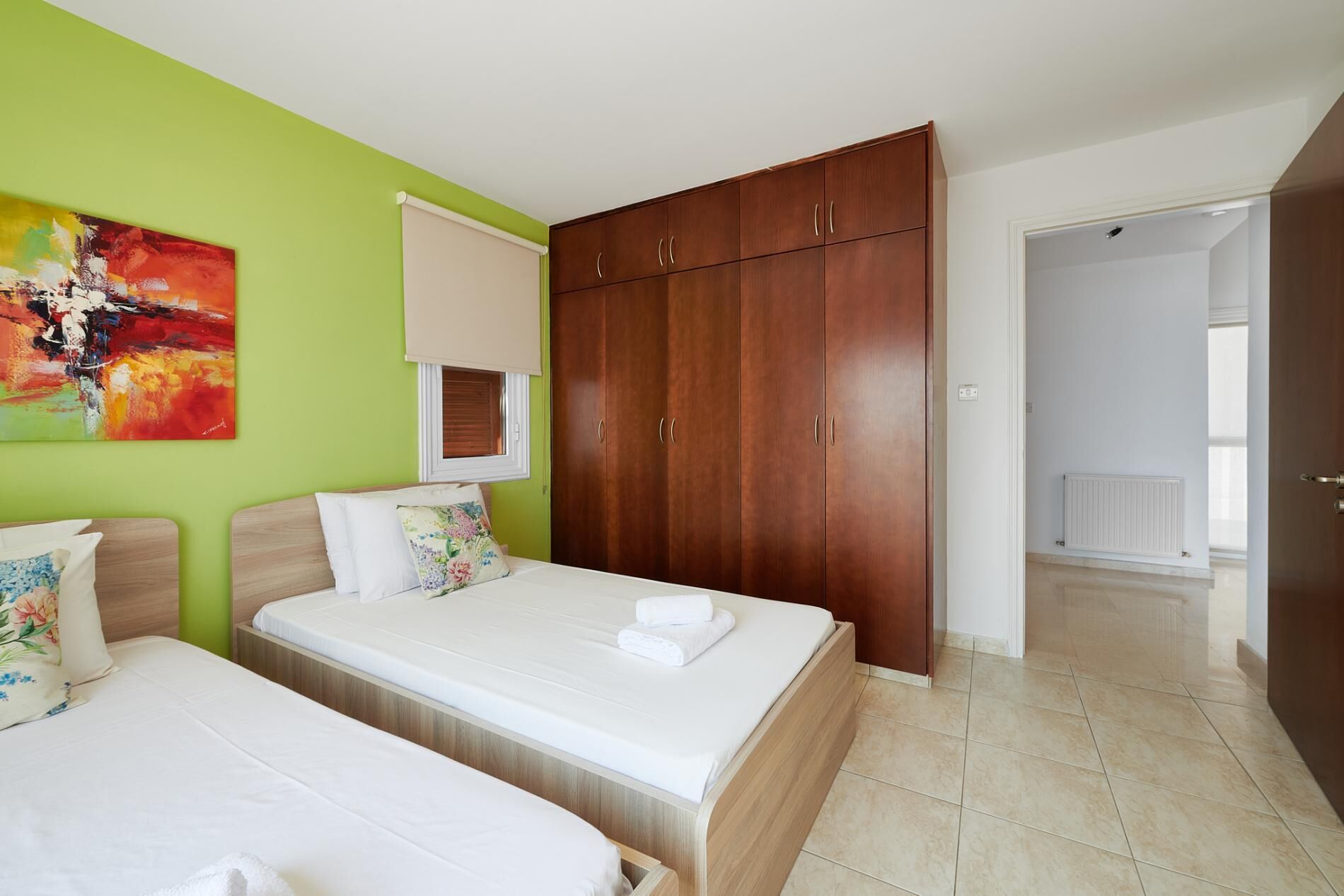Habitació d'hotel amb dos llits, un armari gran, un quadre a la paret i vista al passadís.