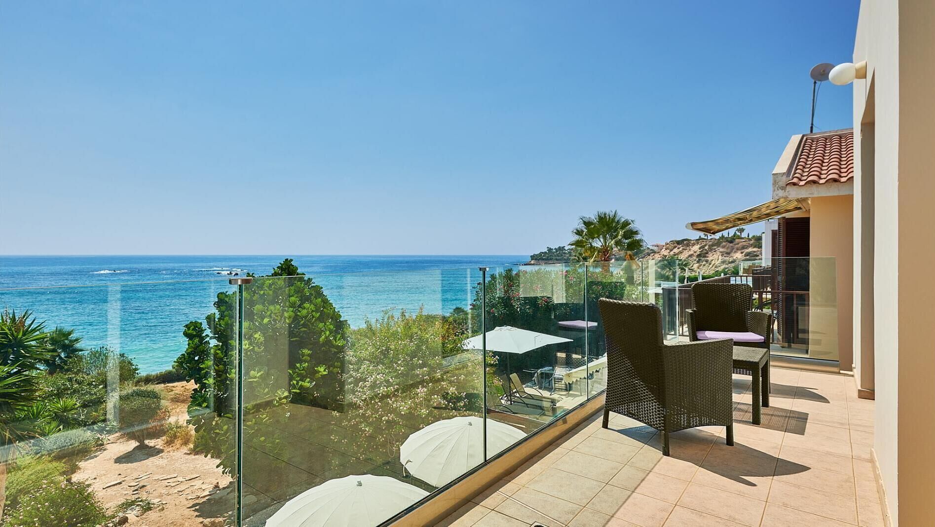 A balcony with a clear view of the sea, wicker furniture, and a glass railing.