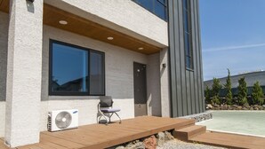 A modern building with a wooden deck, a large window, and an air conditioning unit.