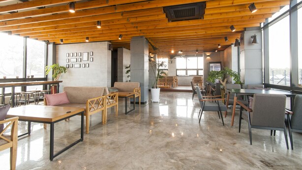 A spacious indoor area with wooden beams, seating arrangements, and large windows allowing natural light.