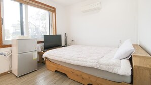 A small, tidy room with a bed, a desk, a refrigerator, a TV, and a window.