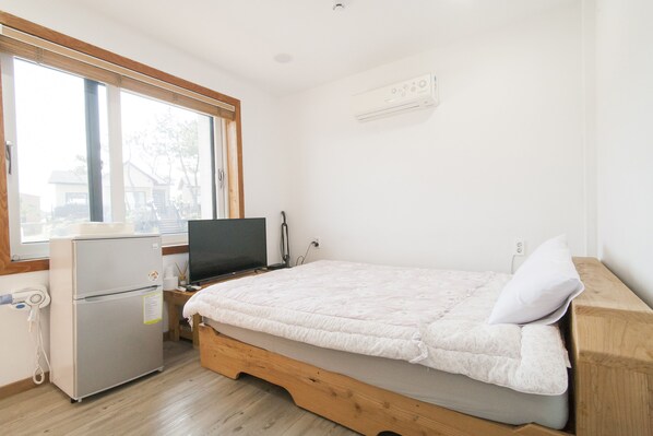 Une petite pièce propre et bien rangée, avec un lit, un bureau, un réfrigérateur, une télévision et une fenêtre.