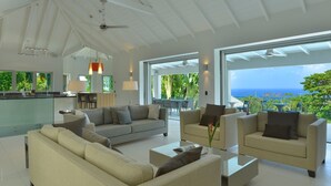 A spacious living area with a large window overlooking the ocean, a kitchen area, and a seating arrangement with sofas and a coffee table. - Family Luxury, Resort Level Amenities, Ocean Views, Perfect Location, Gym. (Jessups)