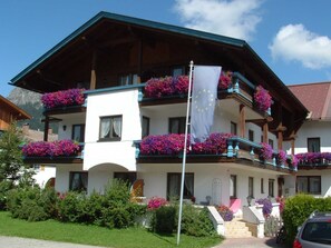 A two-story building with balconies adorned with flowers, a flagpole with a flag, and a clear sky.