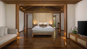 Un dormitorio con una cama grande, vigas de madera, un sofá, un televisor y vistas a un jardín.