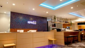 Zona de recepción de hotel con pared de mosaicos, mostrador de recepción y área de descanso.