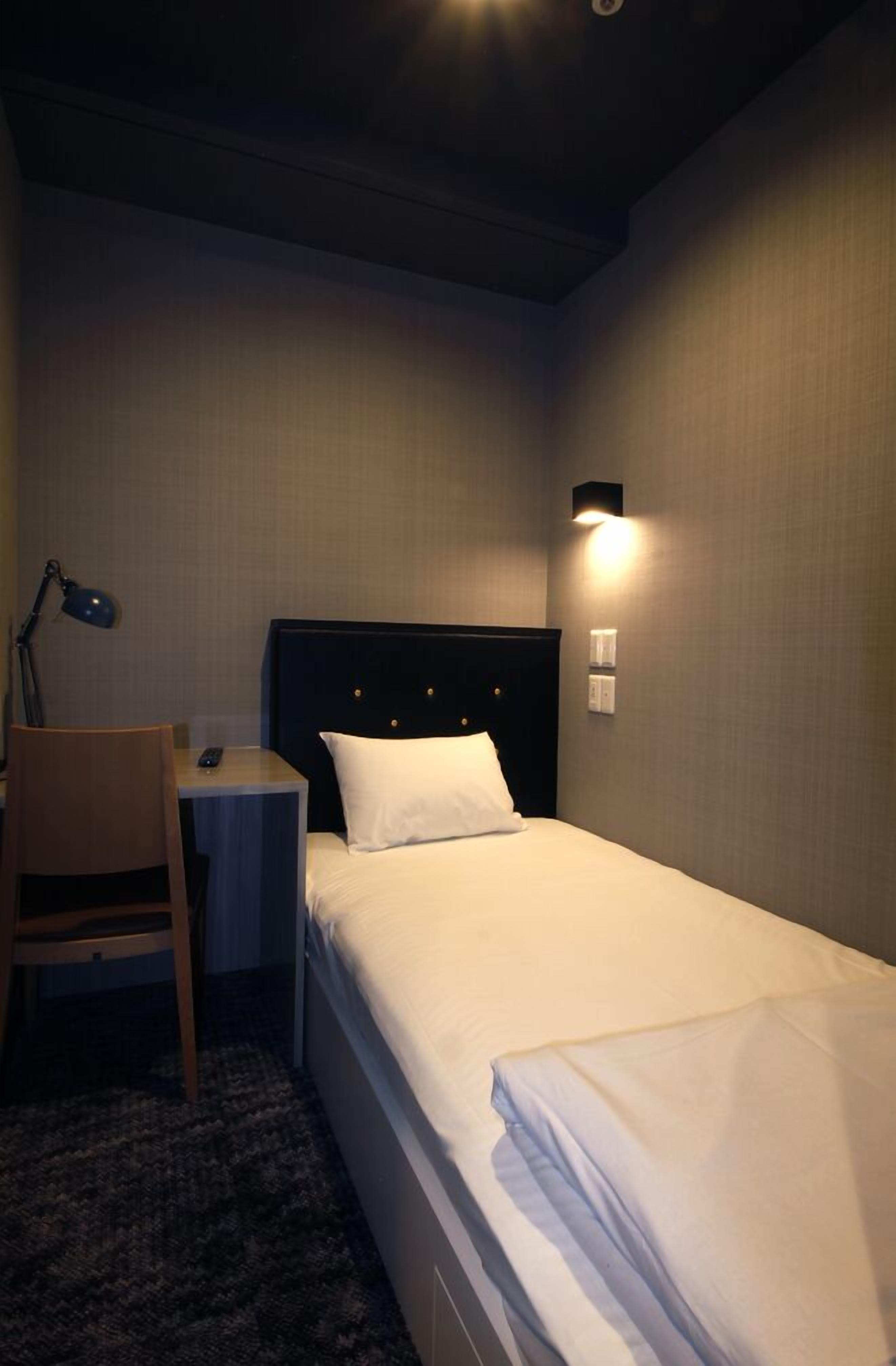 A hotel room with a bed, a desk, a chair, and a lamp.