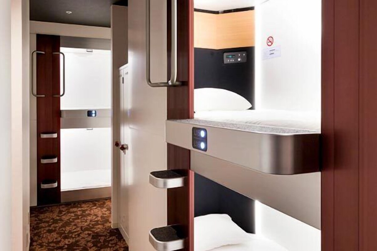 Una habitación de hotel con literas, un panel de control y una puerta que da a otra habitación.