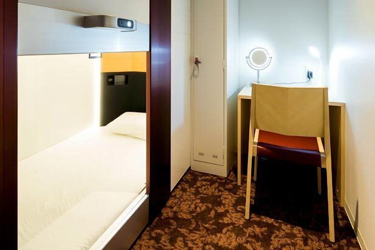 Habitación de hotel con cama, escritorio con silla, una mesita y espejo montado en la pared.