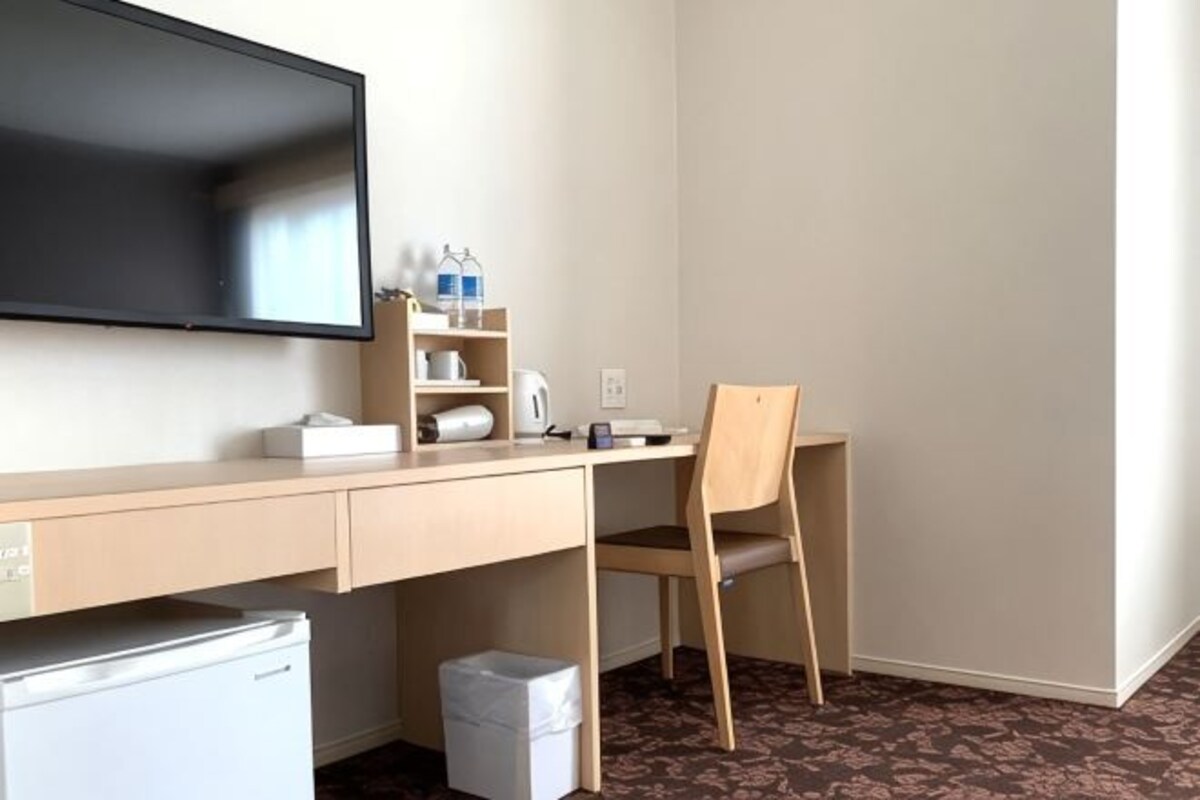 A hotel room with a desk, chair, television, and a small refrigerator.