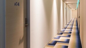 Un largo y estrecho pasillo de hotel con una alfombra estampada y una puerta que indica “A14”.