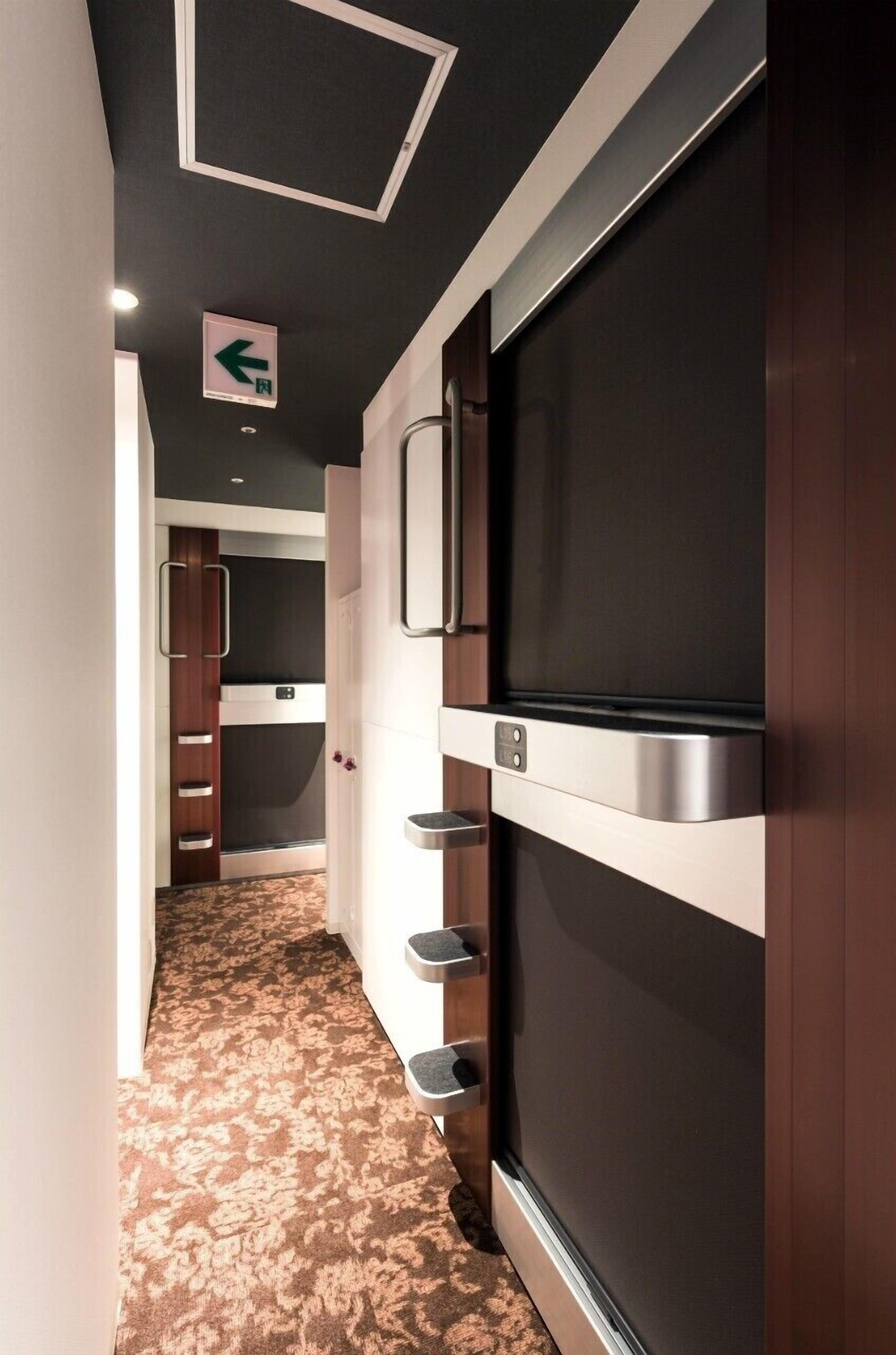 Un pasillo con alfombra estampada, un televisor montado en la pared y una puerta con manija.