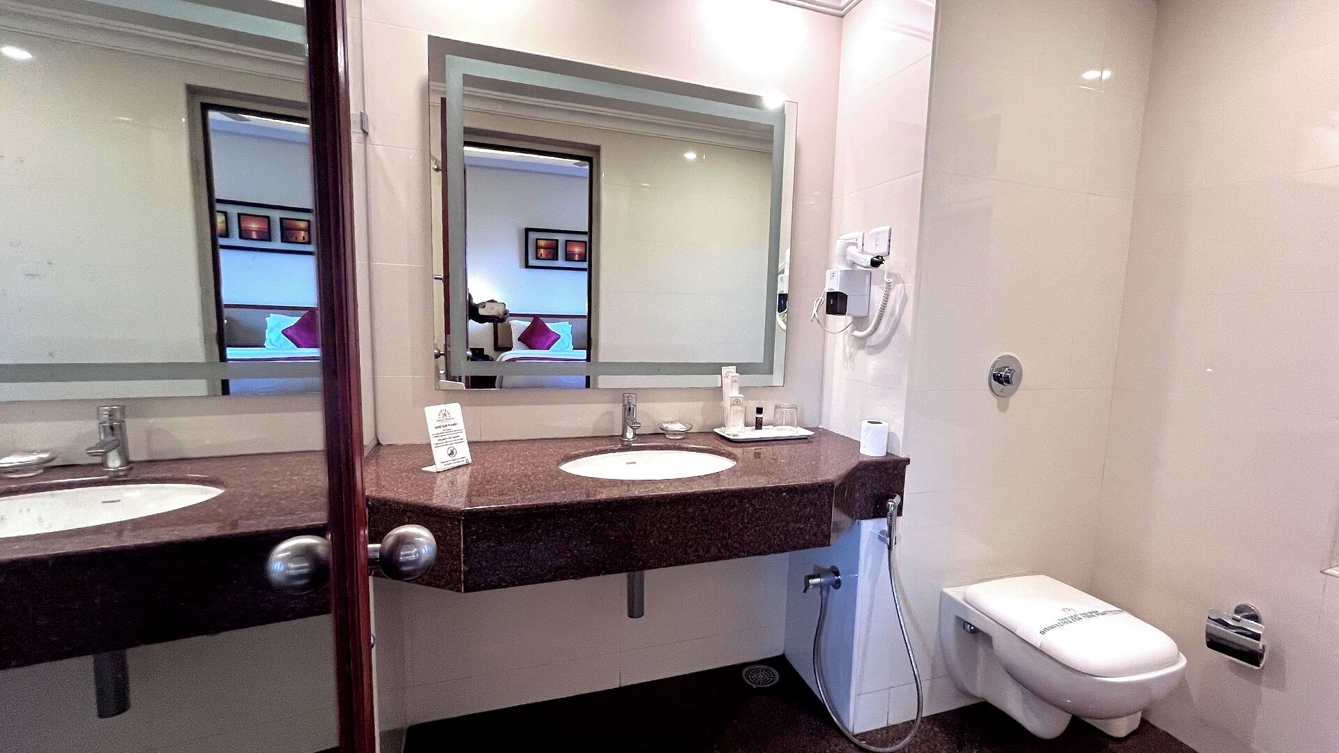 Un baño moderno con dos lavamanos, un espejo, un inodoro y una ducha.