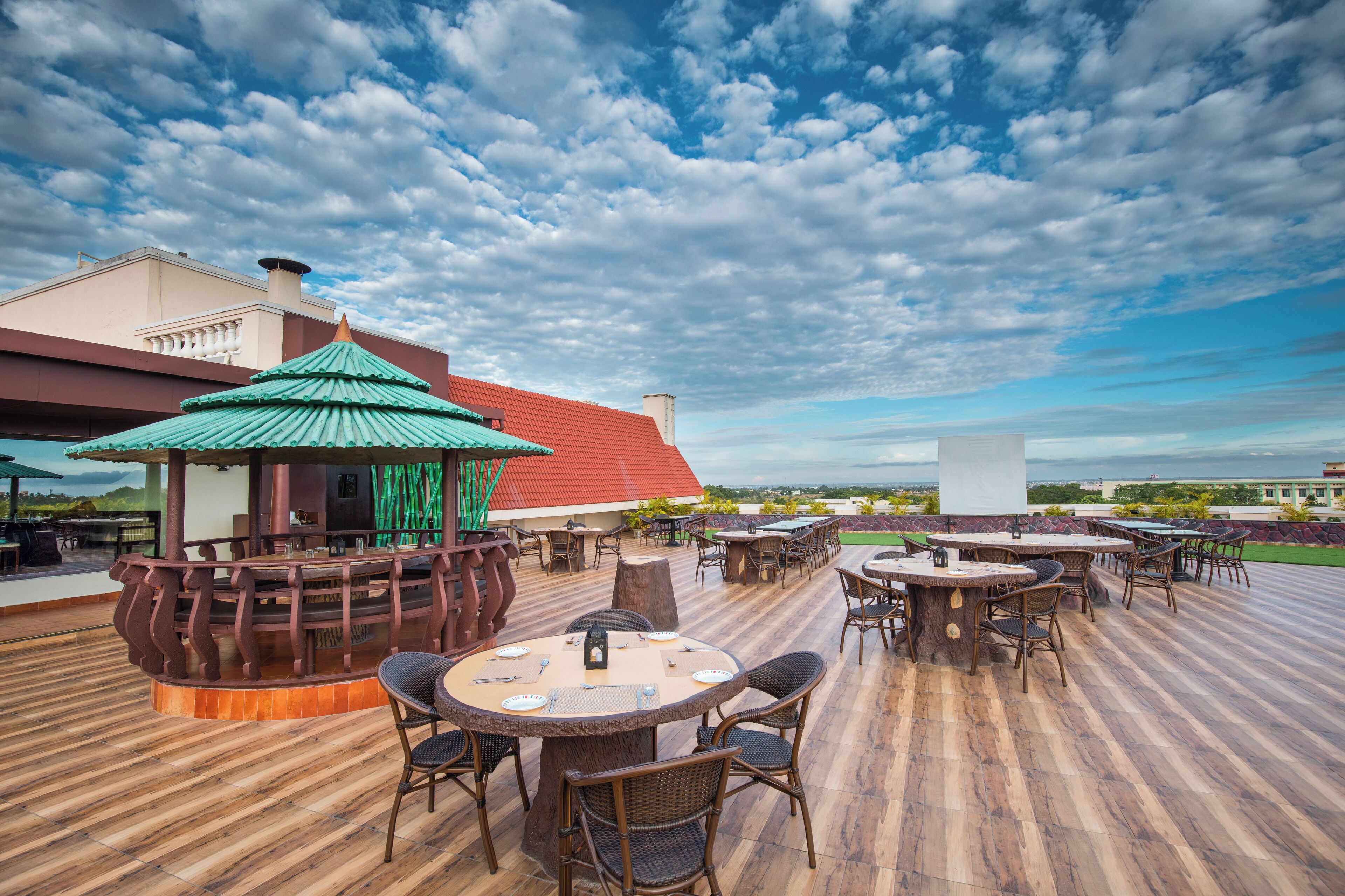 An outdoor patio with round tables and chairs, a gazebo, and a building with a red roof.