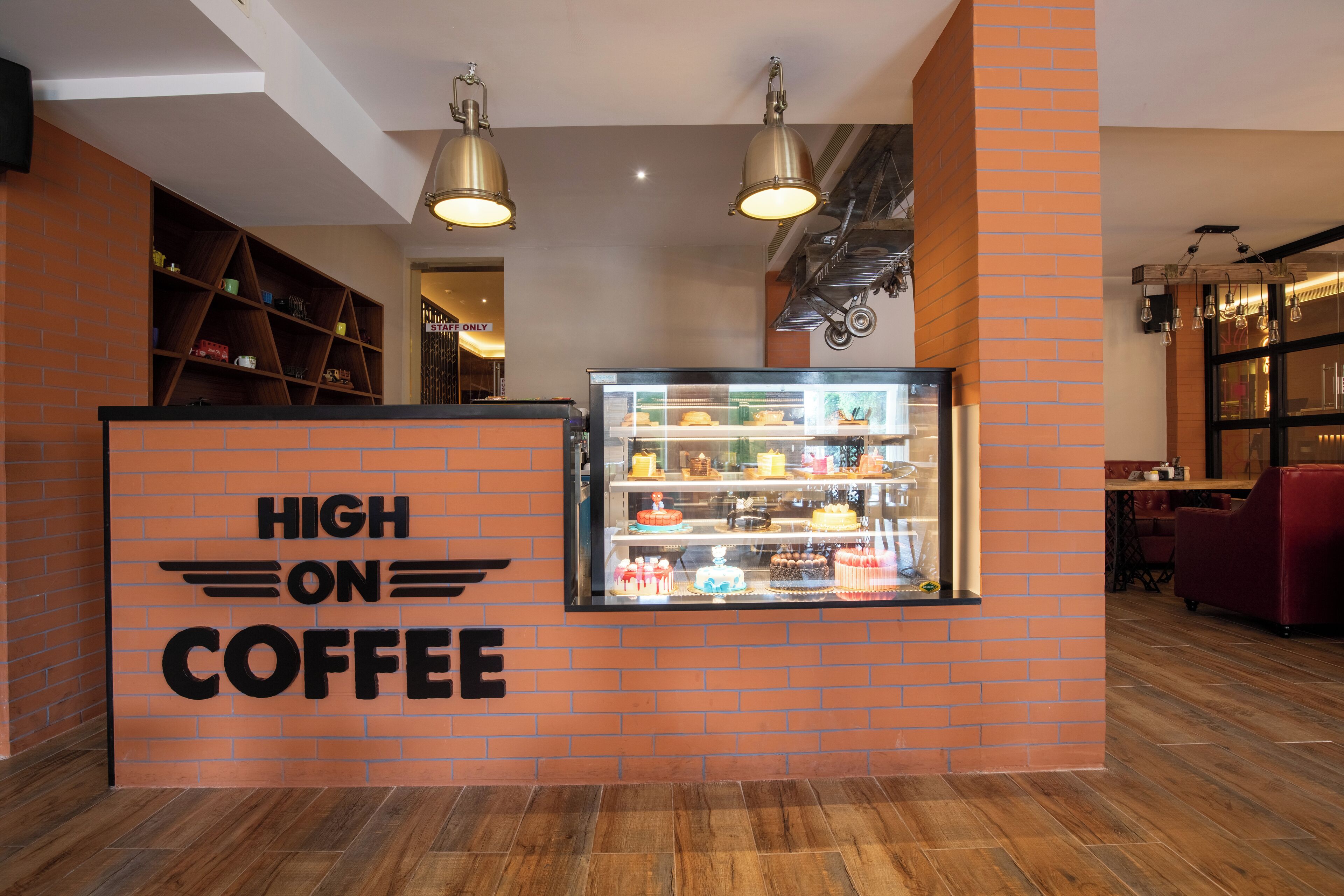 L’intérieur d’un café, avec un mur en briques, une vitrine où sont exposées des pâtisseries et des lampes suspendues.
