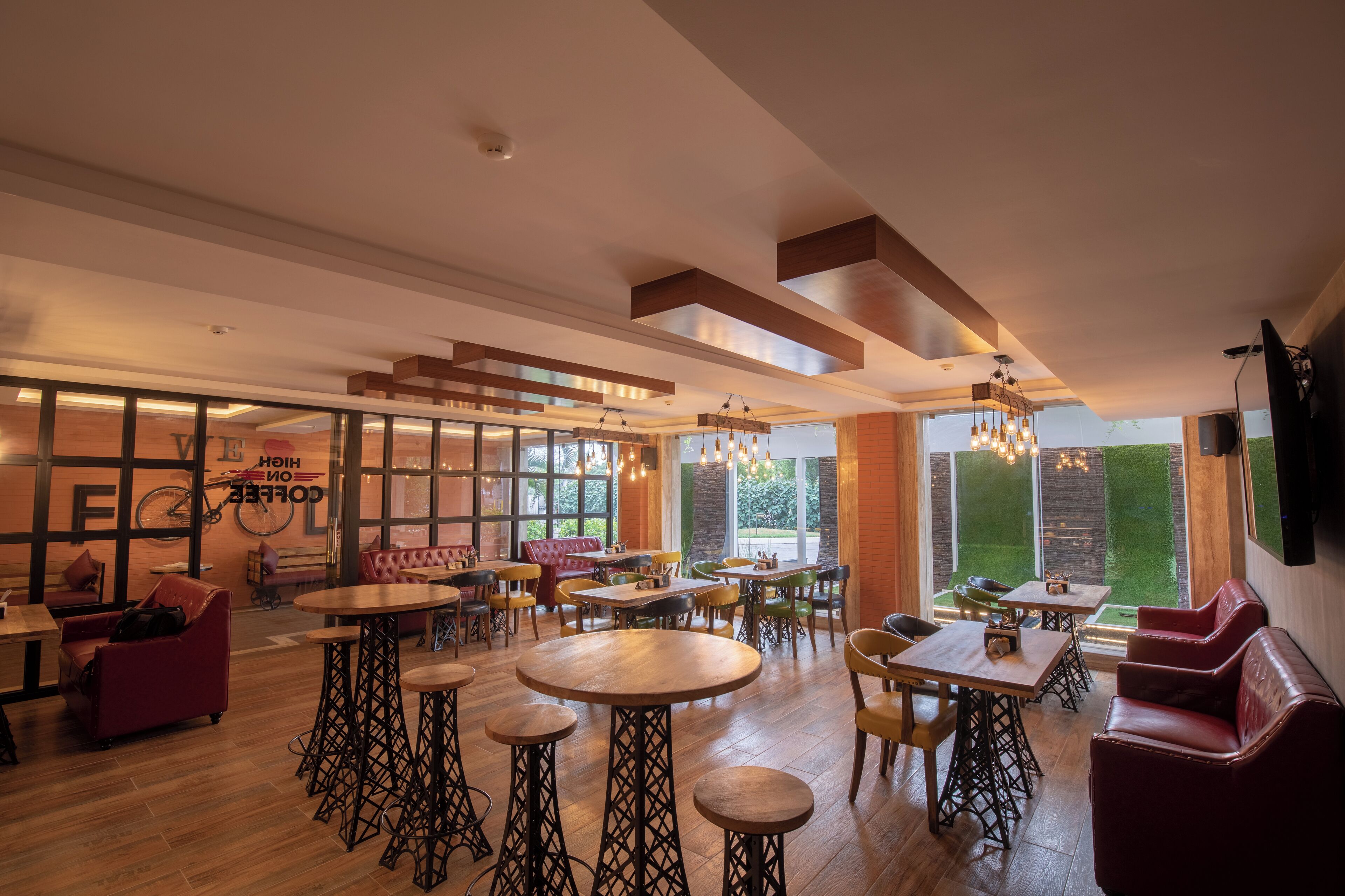 A spacious cafe with wooden tables and chairs, a red sofa, and a large window offering a view of the outdoors.