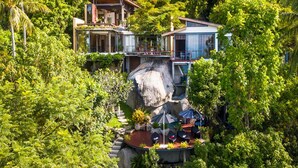 A multi-story house with a large rock feature in the center, surrounded by lush greenery. - L2 Residence (Koh Samui)