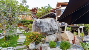 A garden with a wooden deck, a large rock centerpiece, and a small waterfall. - L2 Residence (Koh Samui)