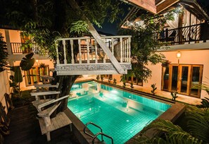A swimming pool with a wooden deck and stairs, surrounded by lush greenery and a building with balconies. - Garden Yard Inn Chiangmai (Chiang Mai)